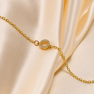 Detail shot of a 18K gold-plated chain with a round zircon pendant on satin fabric