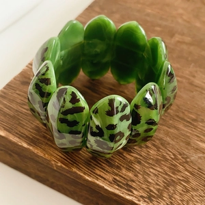 Close-up of green leopard print resin bangle on a natural wooden surface with detailed texture