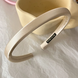 Detail of a thin champagne satin headband with soft sheen and smooth fabric texture