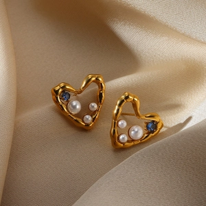 Macro shot of gold heart earring with white pearls and blue zircon on silk