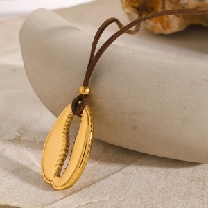 Close-up of golden cowrie shell pendant on a brown cord necklace over stone