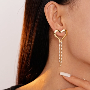 Close-up of heart-shaped gold tassel earrings with sparkling white rhinestones on model