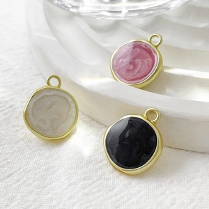 Detail of round enamel disc pendants in pink, beige and black with irregular gold borders