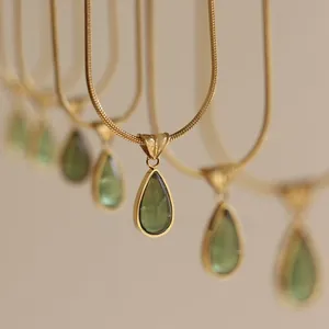 Macro shot of green teardrop pendant with gold snake chain in French vintage style