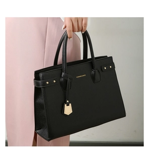 Detail of black pebbled leather tote bag with gold lettering and decorative pendant charm