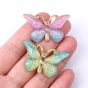 Detailed view of purple and green gradient butterfly charms held by hand for scale