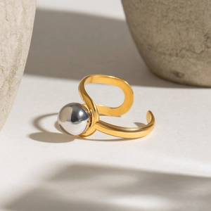 Two-tone gold and silver stainless steel open ring with spherical bead on beige surface