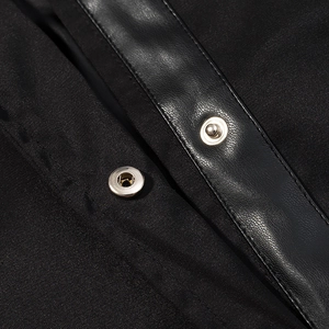 Detail of black trench coat featuring faux leather panels and silver metal snap buttons