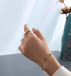 Détail d'une bague dorée 18K et d'un bracelet minimaliste orné de zircons verts