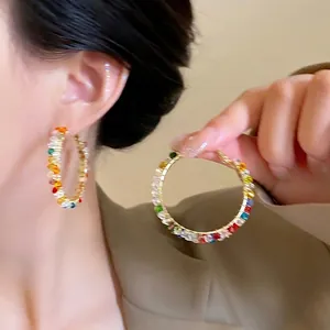 Close-up of oversized gold hoop earrings featuring multi-color gradient crystals and stones