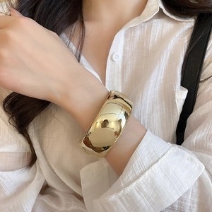 Polished gold wide cuff bracelet with a mirror finish worn on a woman's wrist