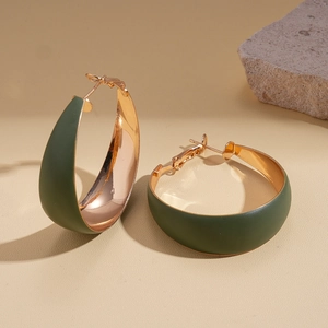 Detail of matte dark green and gold plated geometric hoop earrings on a stone base
