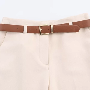 Detail of beige trousers featuring a brown textured belt and a square gold metal buckle