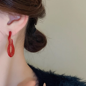 Detail view of deep red wave earrings with high-gloss finish worn by a model