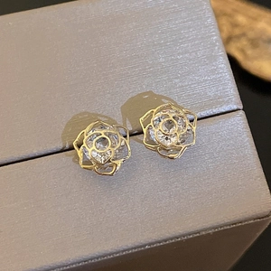 Macro detail of gold rose earrings with clear zircon on textured grey jewelry box
