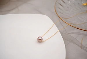 Detail of single round mauve pearl pendant on a thin gold chain against gray fabric
