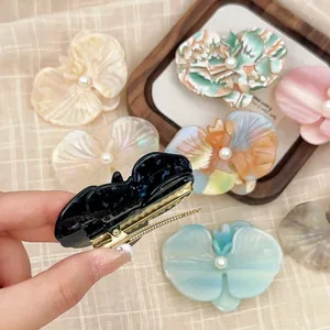 Close-up of orchid acetate hair clips with pearl centers and gold duckbill clips