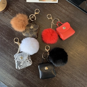 Mini handbag keychains with faux fur pompom in diverse leather textures on wood