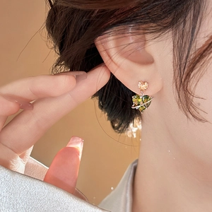 Close-up of heart-shaped green zircon earring with golden orbital ring on a model