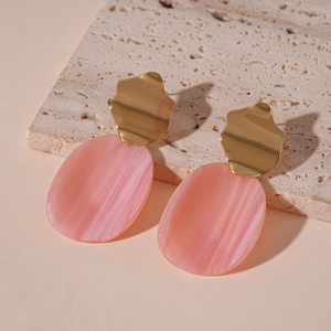 Détail de boucles d'oreilles pendantes en résine rose avec métal doré ondulé élégant