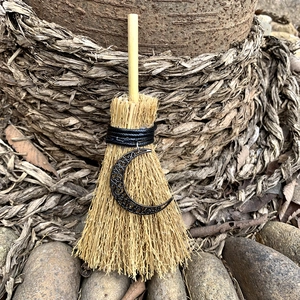 Detailed close-up of a mini witch broom with a crescent moon pendant in a forest setting