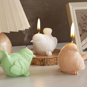 3D bird shaped scented candles in various colors on wooden base with warm lighting