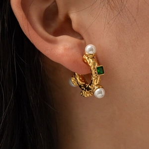 Detail of vintage C-shaped gold earring with green gemstone and white pearls on ear