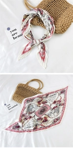 Detail of pleated silk scarf with pink geometric patterns paired with woven straw bag