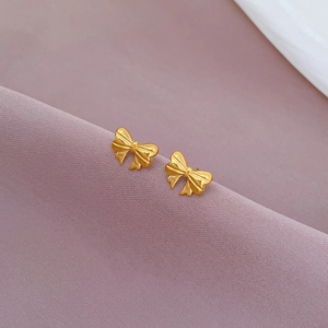 Macro shot of minimalist gold bow earrings on a textured purple fabric background