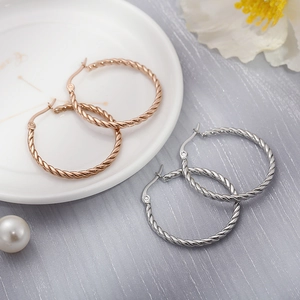 Detail of twisted cable hoop earrings in gold and silver plating on ceramic plate