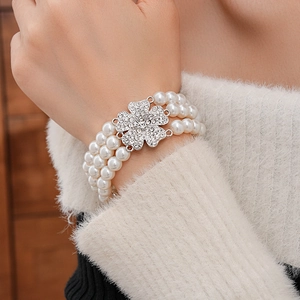 Detail of a multi-layer pearl bracelet with a sparkling rhinestone clover clasp on a model