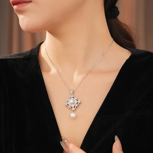 Close-up of a silver zircon diamond flower pendant on a white pearl necklace worn by a model