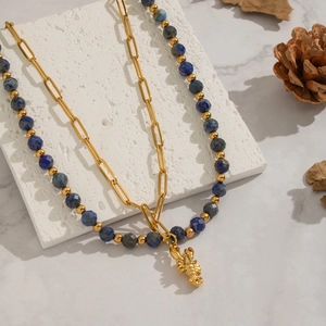 Double-layered gold necklace with lapis lazuli beads and lobster pendant on marble