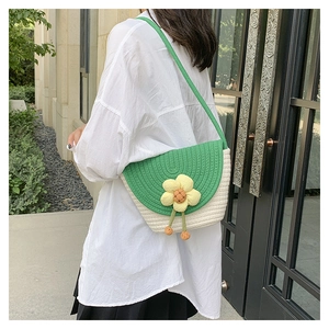 Detailopname van geweven mini schelptas met groene flap en gele bloem op witte blouse
