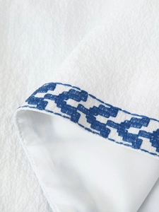 Close-up of white fabric with blue geometric embroidery and textured material details