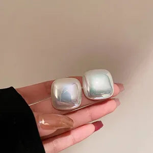 Iridescent square stud earrings with pearl-like luster shown in a close-up hand shot