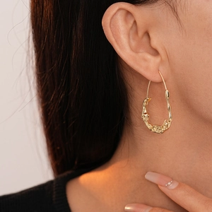 Close-up of a model wearing a gold irregular liquid metal hoop earring with a wavy texture