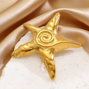 Detail of a polished gold starfish brooch with spiral textures on a white rock background