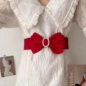 Detailansicht eines roten elastischen Schleifengürtels mit Strassschnalle über weißem Kleid