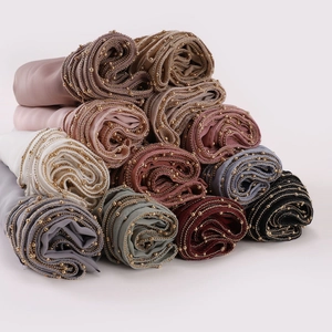 Multiple colorful solid hijabs with decorative gold bead chain edges on white backdrop