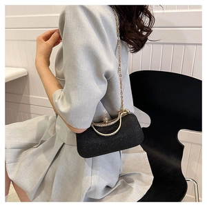 Elegant black glitter evening clutch with gold metal handle held by model on chair