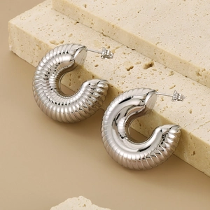 Detailed view of silver hollow caterpillar hoop earrings on textured stone surface