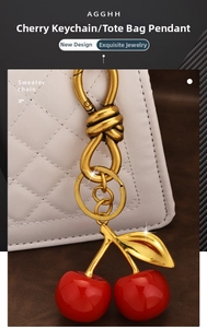 Detailed view of red cherry resin pendant with gold chain hanging on a white quilted bag