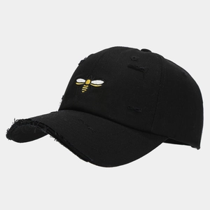 Close-up of small bee embroidery and distressed rip details on a black cotton baseball cap