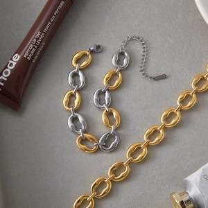 Macro shot of two-tone stainless steel chain bracelet and gold necklace on textured surface