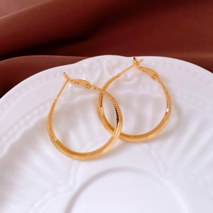 Detail of 18k gold plated hoop earrings featuring a textured surface on a white relief plate