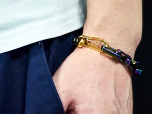 Detail view of rainbow and gold chain bracelet with a spring clasp on a male wrist