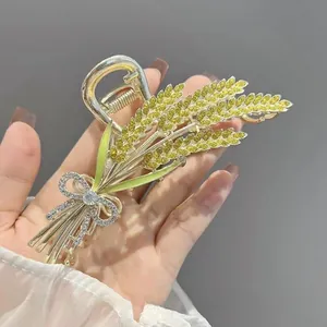 Detailed close-up of golden wheat stalk hair claw clip with green enamel and crystal bow
