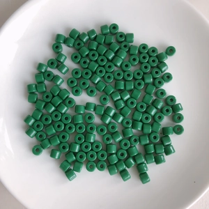 Macro shot of forest green cylindrical acrylic beads with glossy finish on a white plate