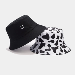 Close-up of a black smiley face bucket hat and a cow print pattern sun hat made of cotton